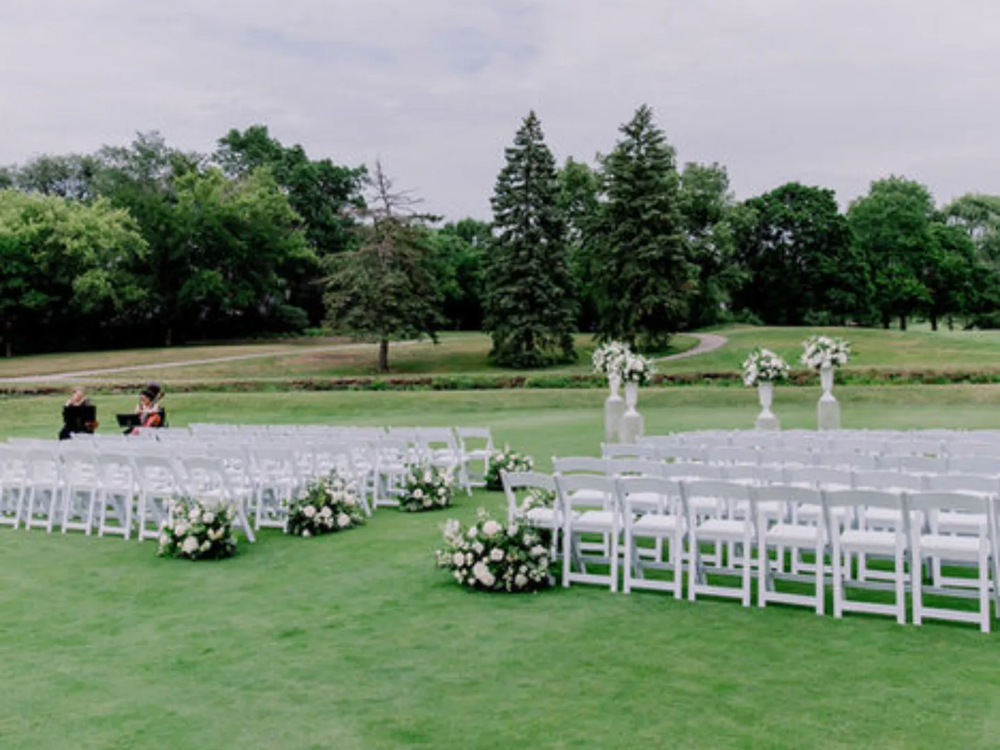 Rows of white folding chairs and floral aisle markers set up for a ceremony on the golf course lawn