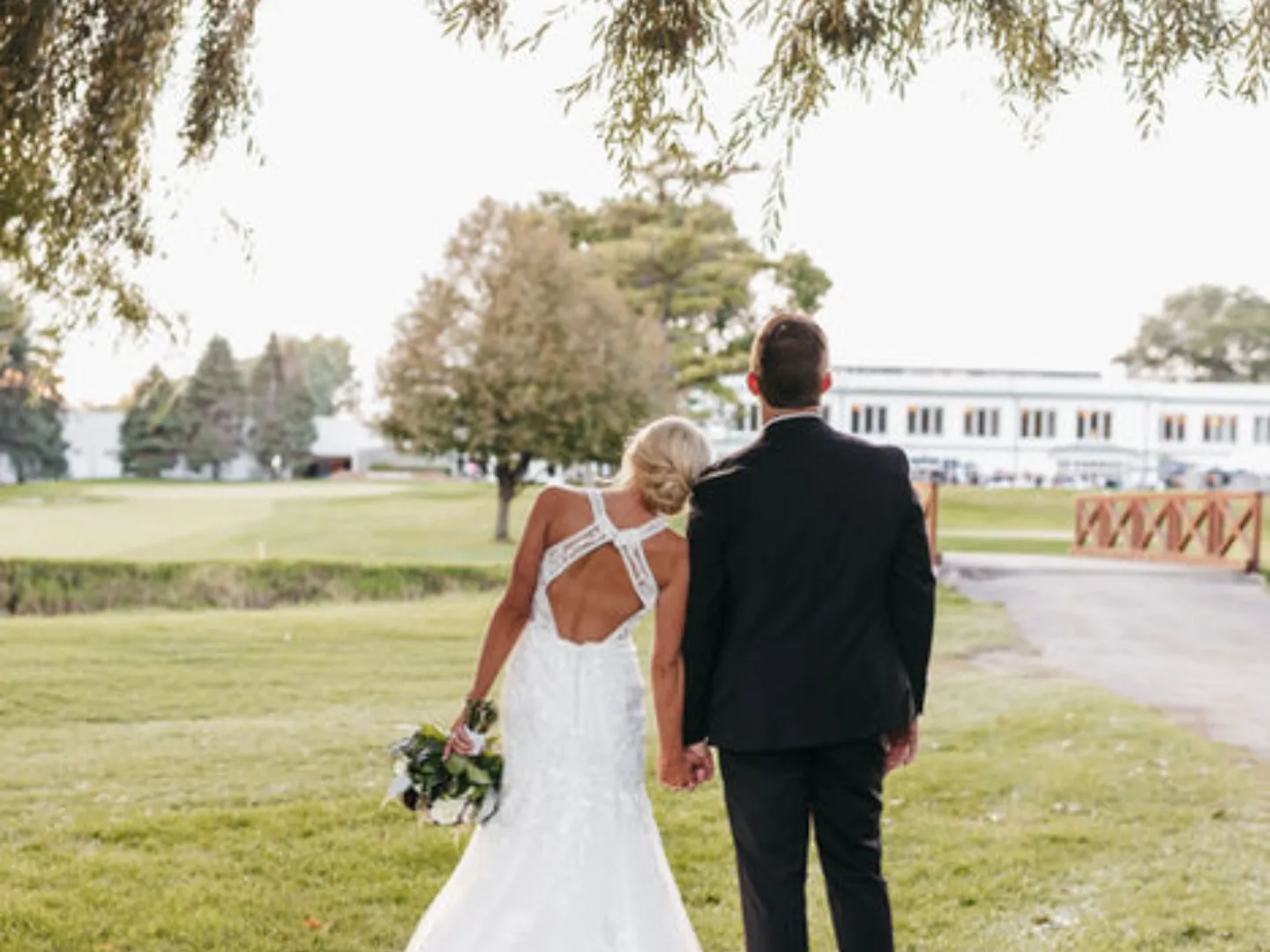 A couple walks hand in hand across the lawn toward the white clubhouse