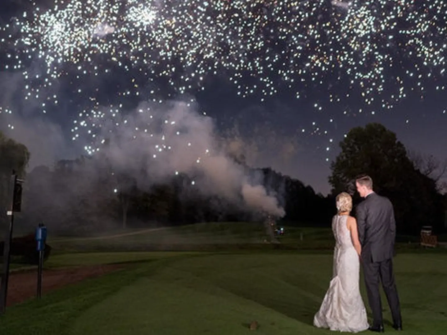 A couple stands on the dark course beneath a shower of sparks
