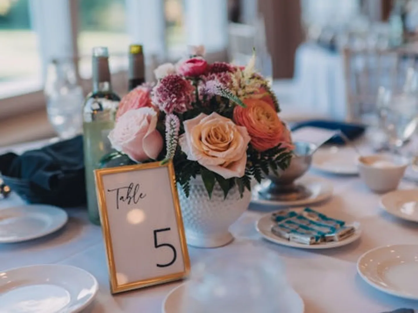 A reception table with a peach and pink centerpiece and a gold table number
