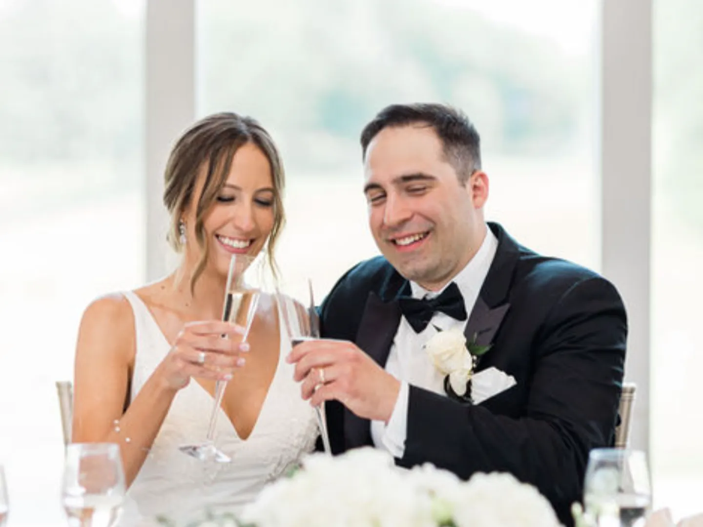 A bride and groom raise champagne glasses at their table