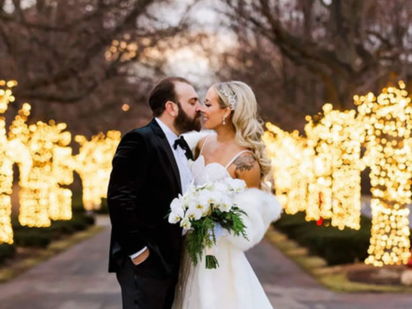 A couple kisses on a path lined with glowing string lights